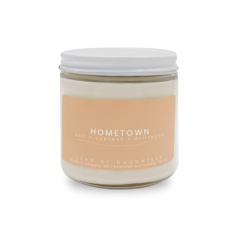 16oz glass jar candle with white lid and a beige label that reads Hometown, salt + cypress + driftwood on a white background