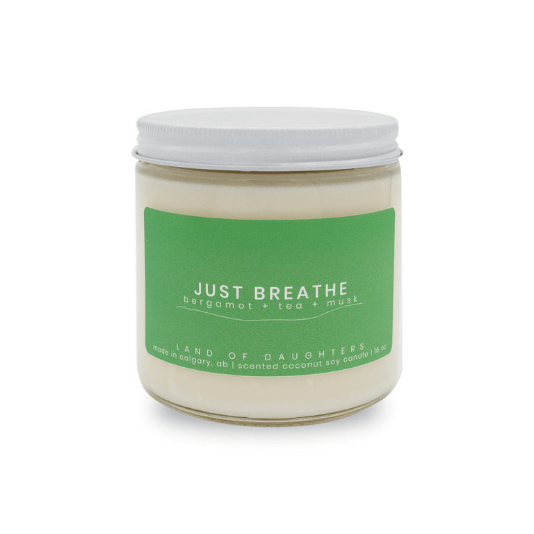 A 16oz glass jar candle with a green label that reads Just Breathe, bergamot + tea + musk photographed on a white background.
