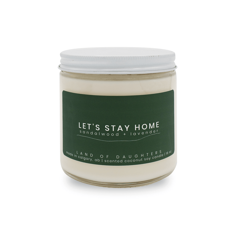 16oz Glass Jar candle with white lid and a dark green label that reads Let's Stay Home, sandalwood + lavender is photographed on a white background.