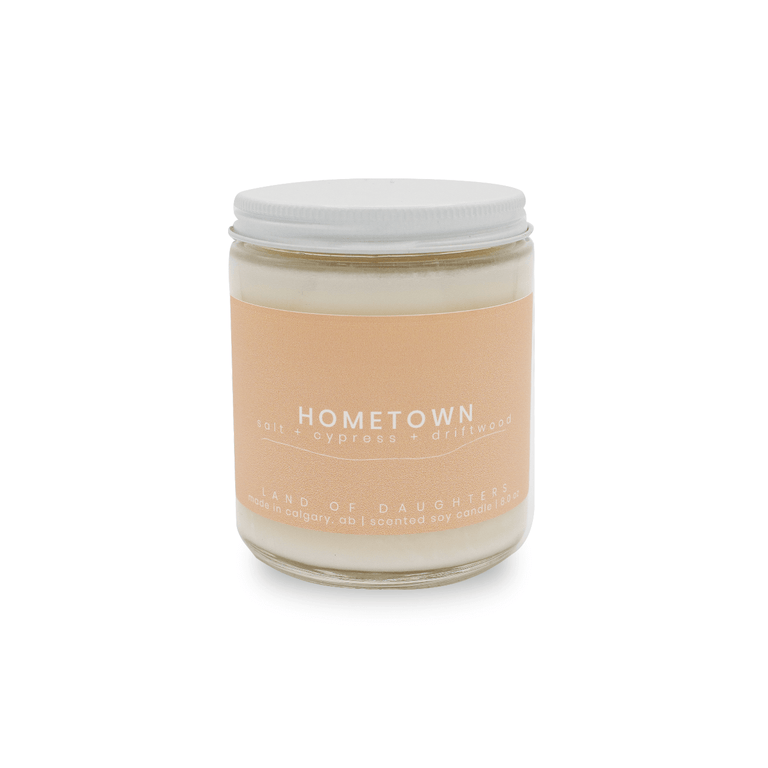 8oz glass jar candle with white lid and a beige label that reads Hometown, salt + cypress + driftwood on a white background