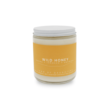8oz Glass Jar candle with white lid and a light orange label that reads Wild Honey, honey + tobacco + oak moss is photographed on a white background.