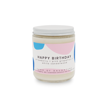 a glass jar candle with a pink and blue label that reads Happy Birthday, strawberry + pink grapefruit + white sandalwood on a white background