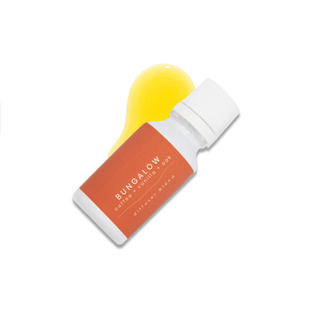 a small white glass bottle with a burnt orange label that reads Bungalow, coffee + vanilla + oak rests upon a pool of fragrance oil