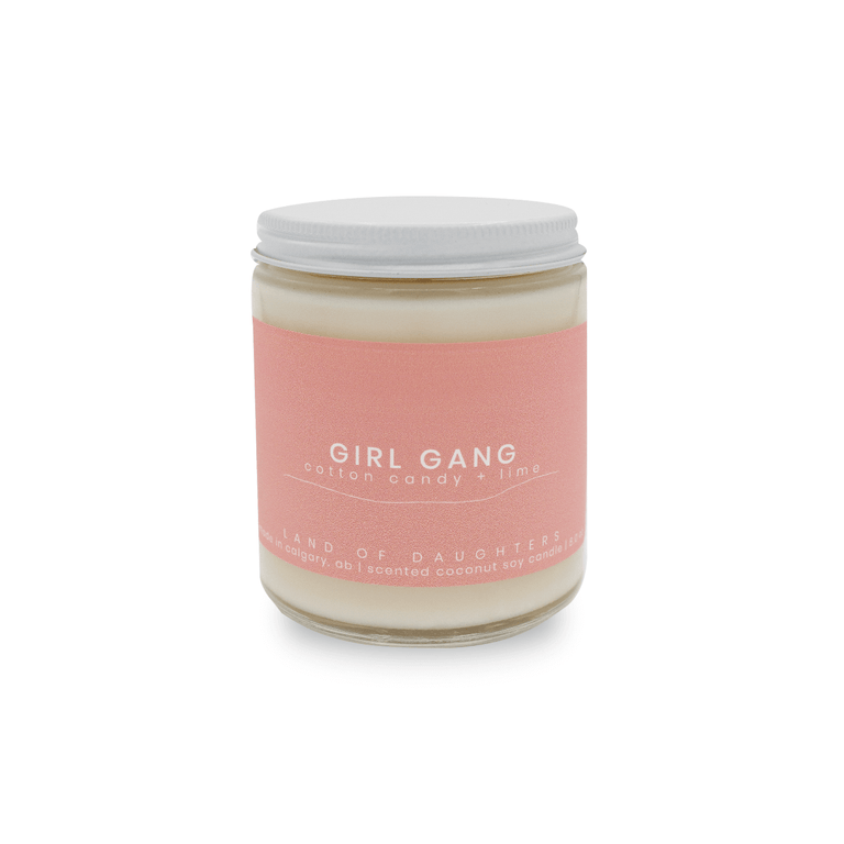 a 8oz glass jar candle with a white lid and a light pink label reading Girl Gang, cotton candy + lime on a white background.