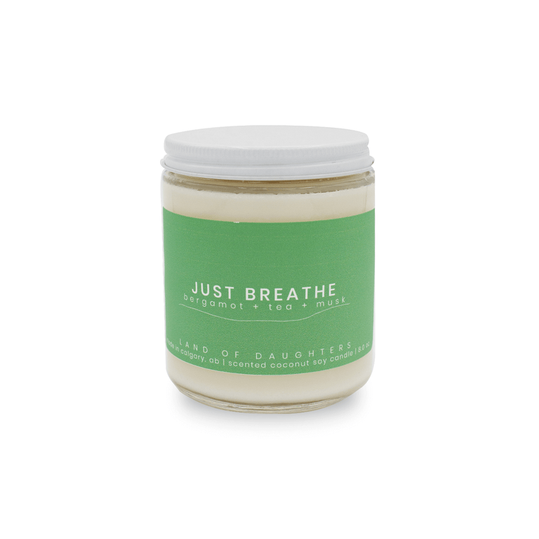 An 8oz glass jar candle with a green label that reads Just Breathe, bergamot + tea + musk photographed on a white background.