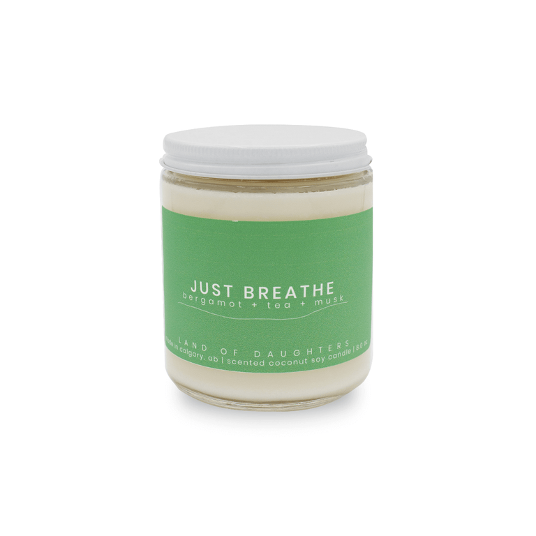 An 8oz glass jar candle with a green label that reads Just Breathe, bergamot + tea + musk photographed on a white background.