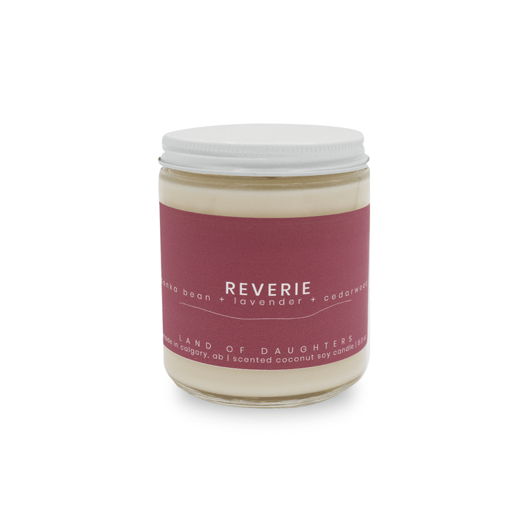 8oz Glass Jar candle with white lid and a dark purple label that reads Reverie, tonka bean + lavender + cedarwood is photographed on a white background.