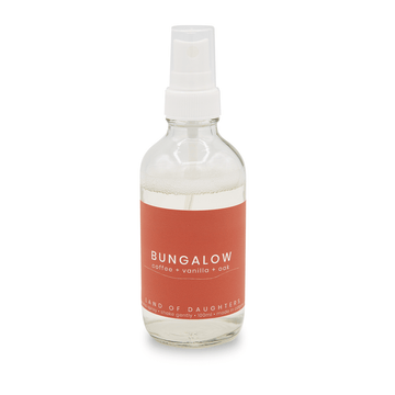 Glass aroma spray bottle filled with liquid with a burnt orange label reading Bungalow, coffee + vanilla + oak on a white background