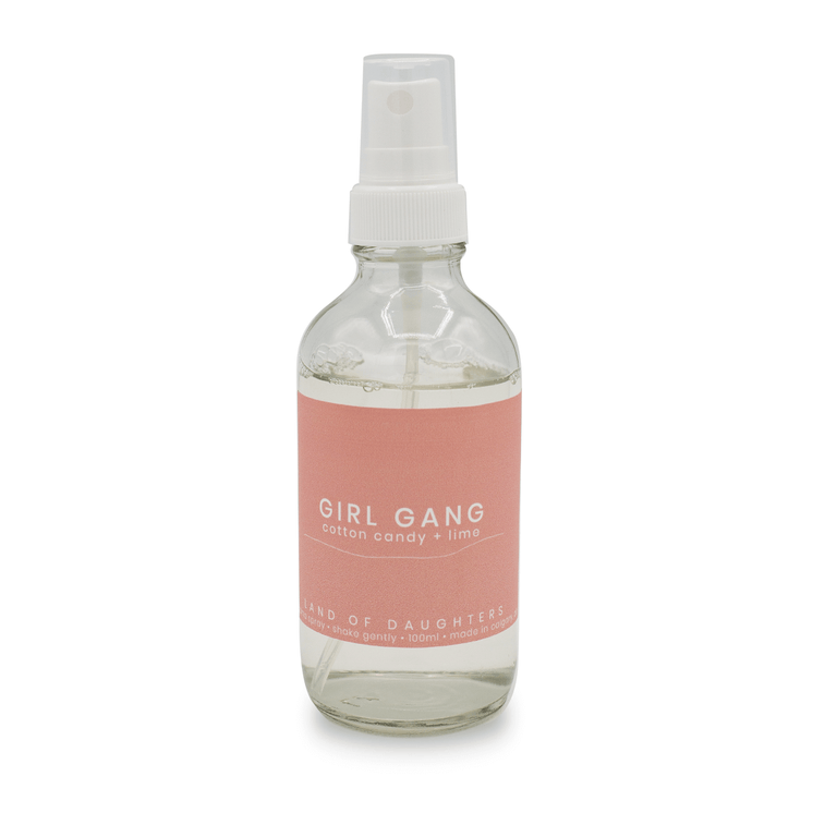 A glass aroma spray bottle with a light pink label that reads Girl Gang, cotton candy + lime on a white background.