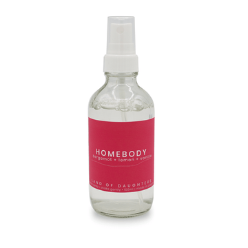 A glass aroma spray bottle with a deep pink label that reads Homebody, bergamot + lemon + vanilla on a white background.