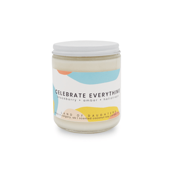 glass jar candle with white lid and blue and yellow label reading Celebrate Everything, blackberry + amber + heliotrope on a white background.