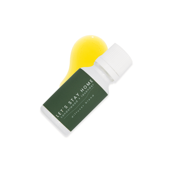 A small white glass bottle with white lid and a dark green label that reads Let's Stay Home, sandalwood + lavender rests upon a small pool of fragrance oil on a white background.